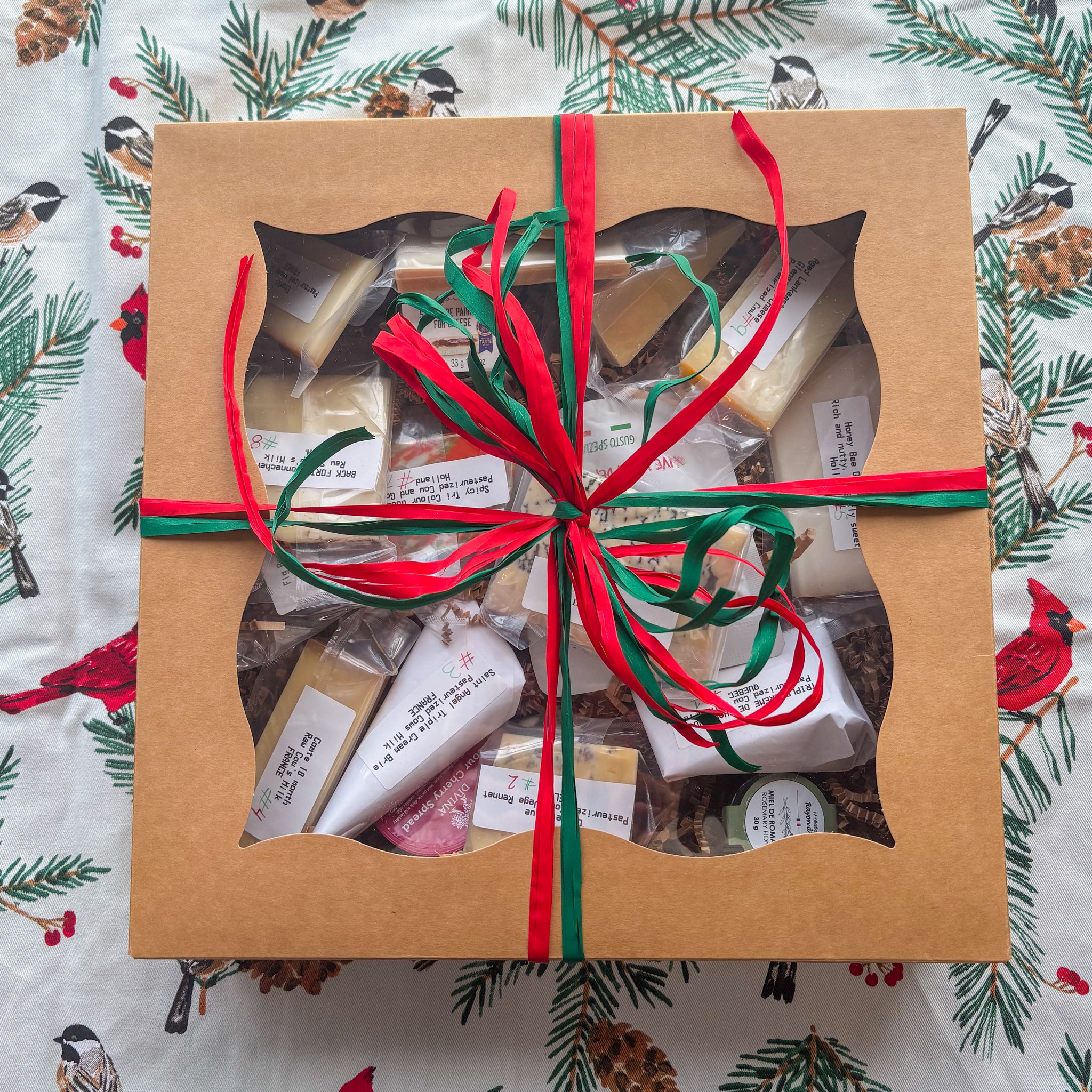 Gift box with a variety of items wrapped in brown paper with red and green ribbons on a festive background.
