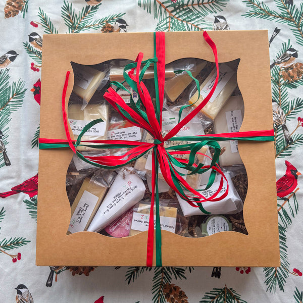 Gift box with a variety of items wrapped in brown paper with red and green ribbons on a festive background.